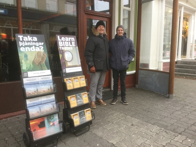 Two people standing next to a stand with religious literature on a city street.