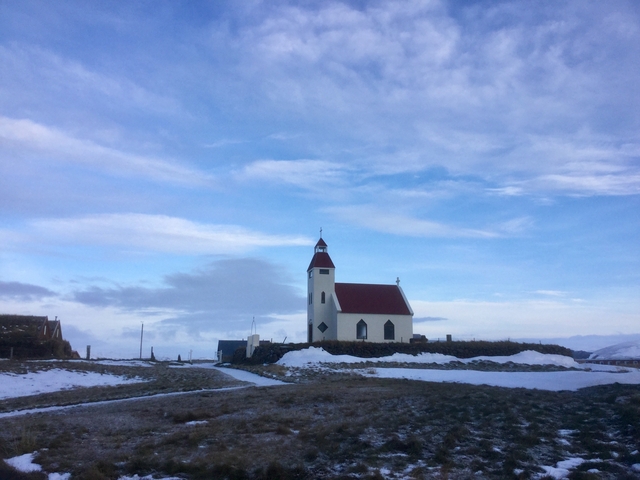 A small church with a red roof in a snow-covered landscape under a blue sky.