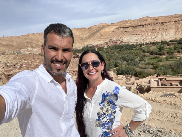 Two people posing with a desert village in the background.
