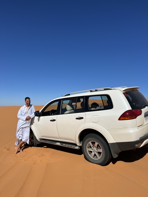 Man posing next to a white SUV in the desert.
