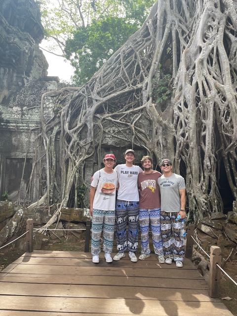 Four people standing in front of a temple with tree roots.