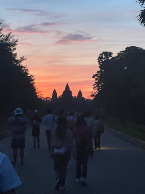 Silhouetted people walking towards Angkor Wat at sunset.