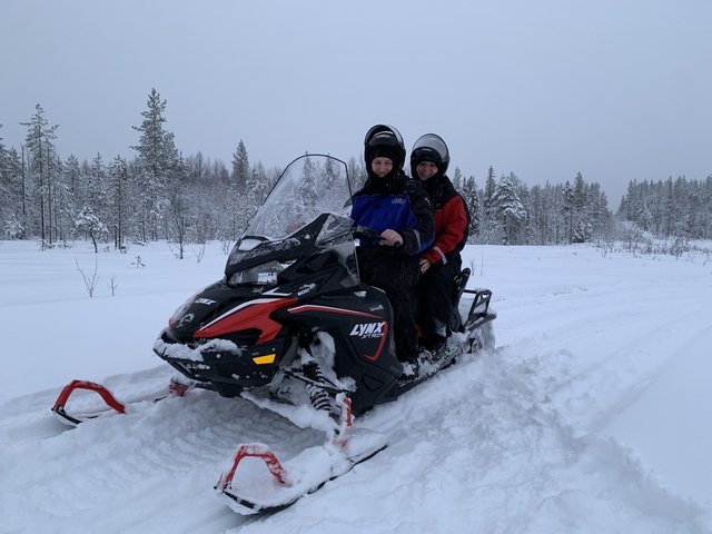 Two people on a snowmobile in the snow.