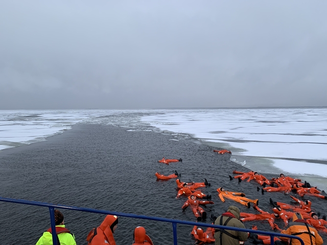 People in orange suits floating in icy water.