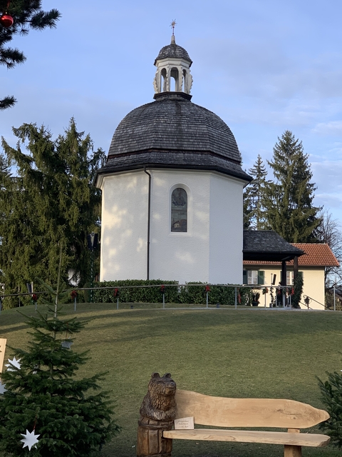 Small, historic chapel surrounded by trees and a garden.