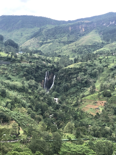Waterfall nestled in a green, hilly landscape.