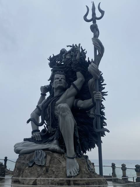 Monumental statue of a deity holding a trident, surrounded by engraved details.