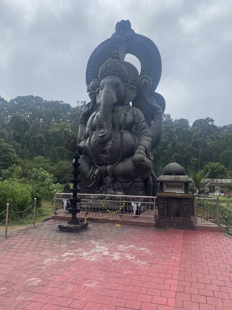 Large statue of Lord Ganesha on a red platform surrounded by vegetation.