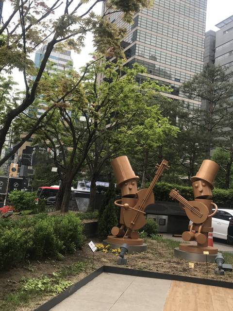 Artistic sculptures in a park with buildings in the background.