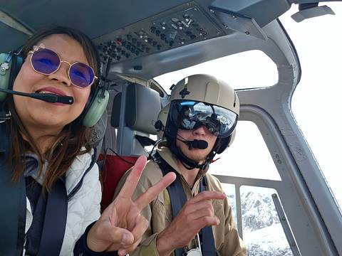 Two people in a helicopter cockpit smiling.
