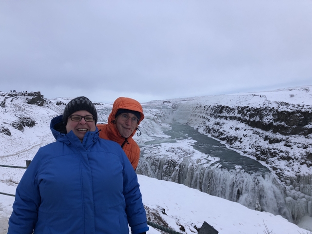 Two people in winter clothing posing with a snowy waterfall in the background.
