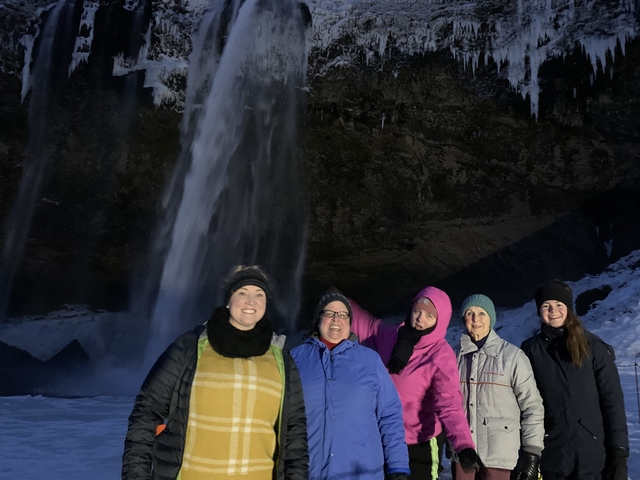 A group of people in winter clothing posing in front of a nighttime waterfall.