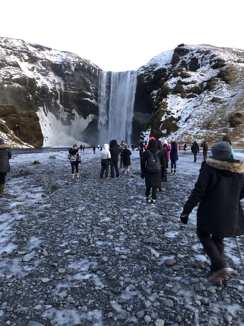 A group of people walking towards a large waterfall.