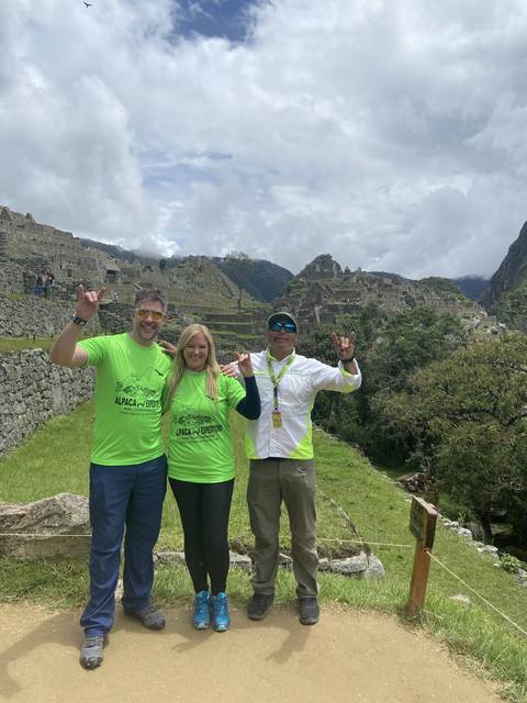 Three people wearing matching shirts posing in front of Machu Picchu.
