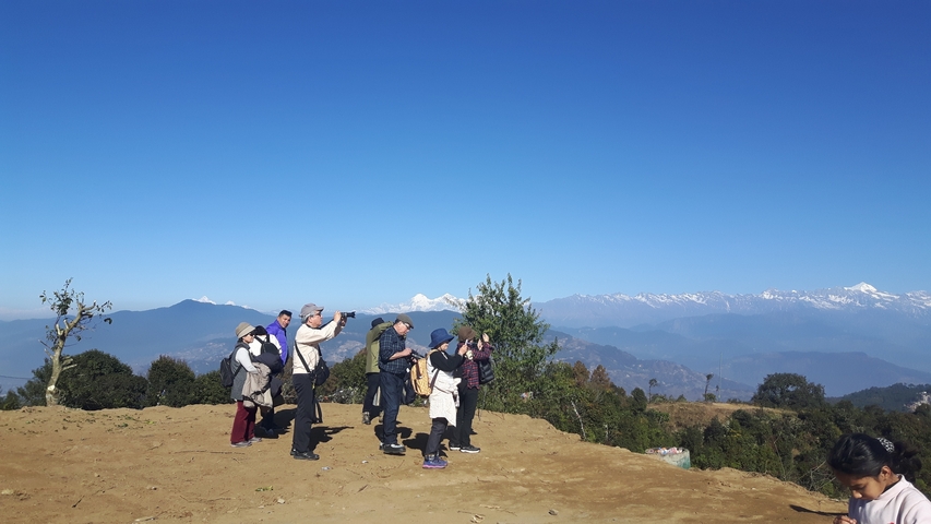 People pointing and taking photos with mountains in background.
