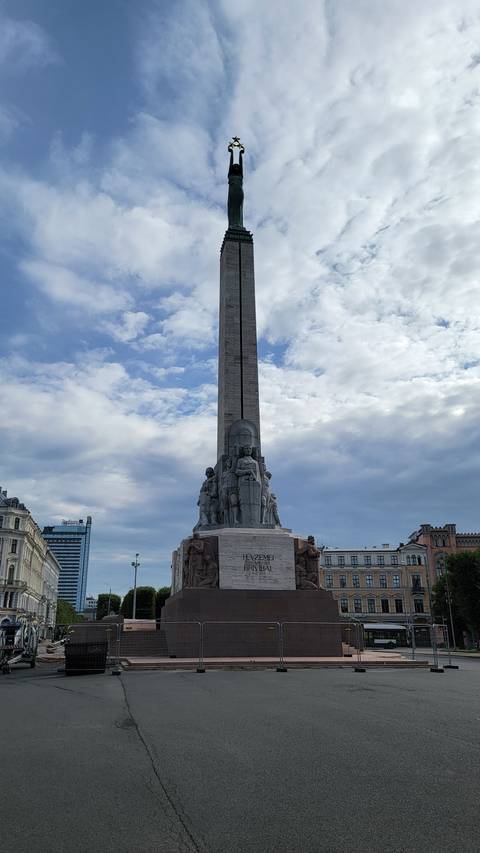 A tall statue with a figure on top, surrounded by buildings.