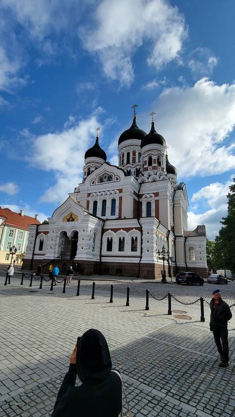 A large white church with black domes and people walking nearby.