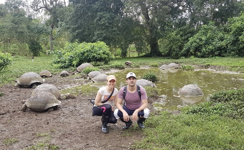 Two people posing in front of a pool with giant tortoises