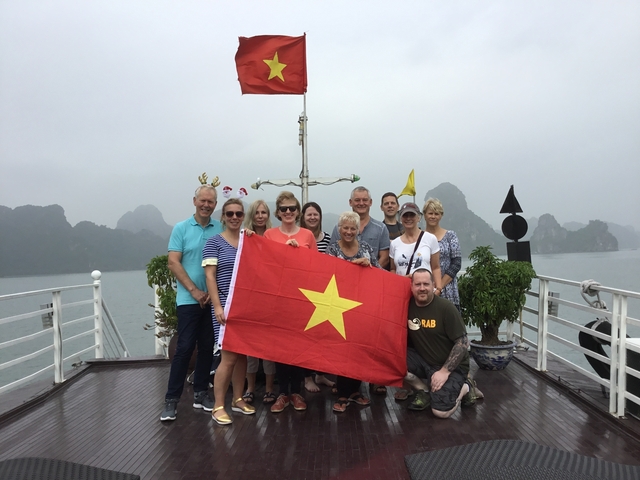 Group holding Vietnam flag on a boat with misty mountains.