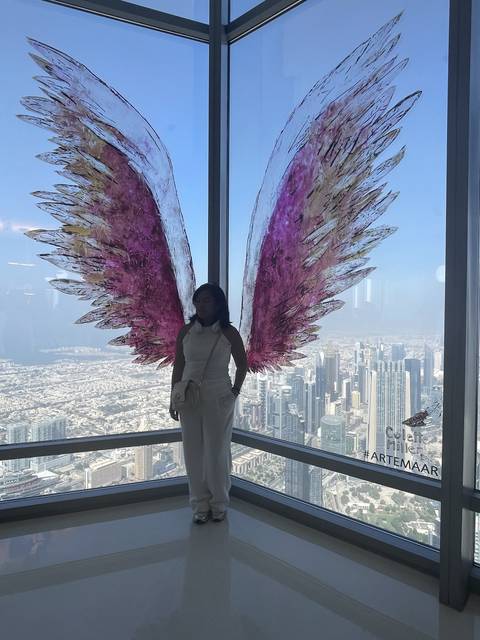 Woman posing in front of colorful wings and a cityscape.