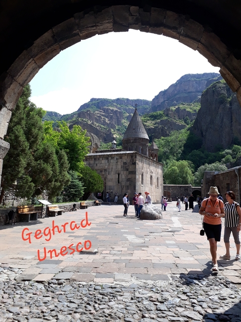 Monastery courtyard with tourists, carved into a rocky canyon.