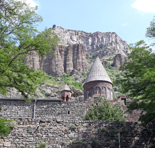 Close-up of a stone building with a conical roof amidst cliffs.