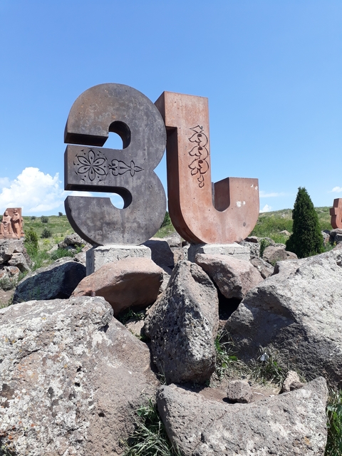 Large stone letters with decorative carvings in a garden setting.