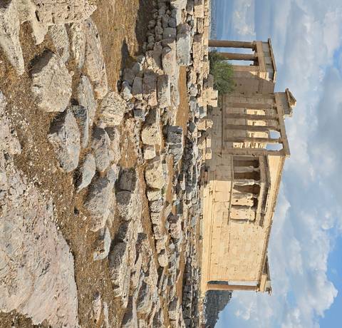 Ancient ruins with columns and rocks in foreground.
