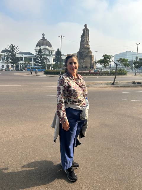 Woman standing on a paved area with statue in the background.