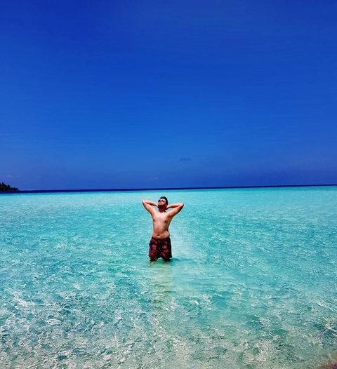Person standing in calm turquoise water with a clear sky.