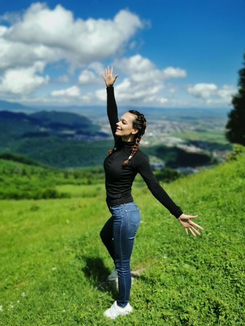 A person joyfully posing with a scenic hilly landscape in the background.
