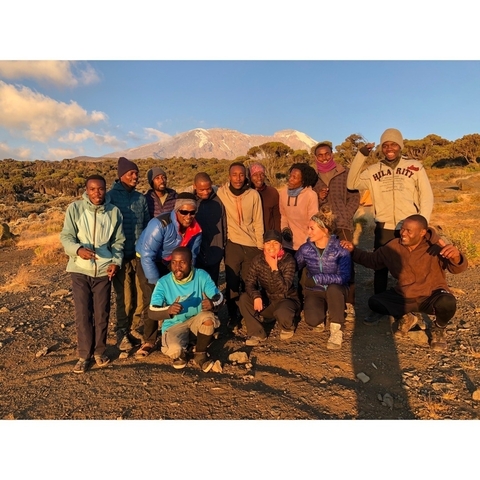 Large trekking team poses at sunrise with Mount Kilimanjaro snowcap glowing behind