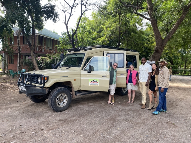 Safari group stands in front of beige Land Cruiser beneath shady trees