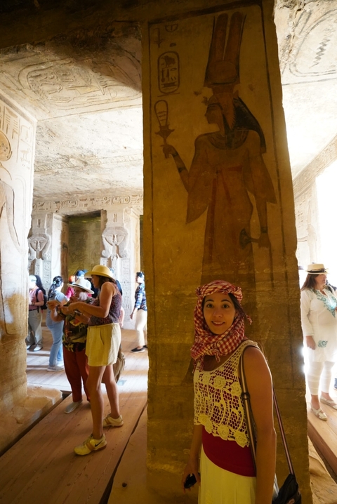 Visitors explore the hieroglyph-covered halls of an ancient Egyptian temple interior under diffused light.