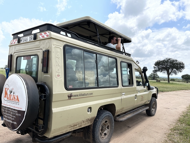 Person using binoculars from the roof of a safari vehicle.
