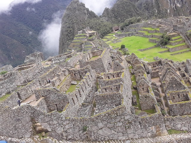 Panoramic overhead view of the stone citadel and terraces of Machu Picchu surrounded by green slopes and drifting cloud.