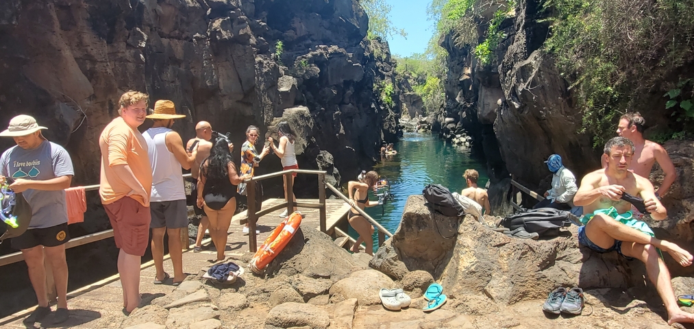 People gathered around a rock-lined pool, some swimming.