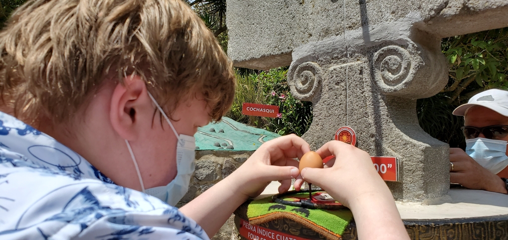 Individual balancing an egg on a monument with signage.