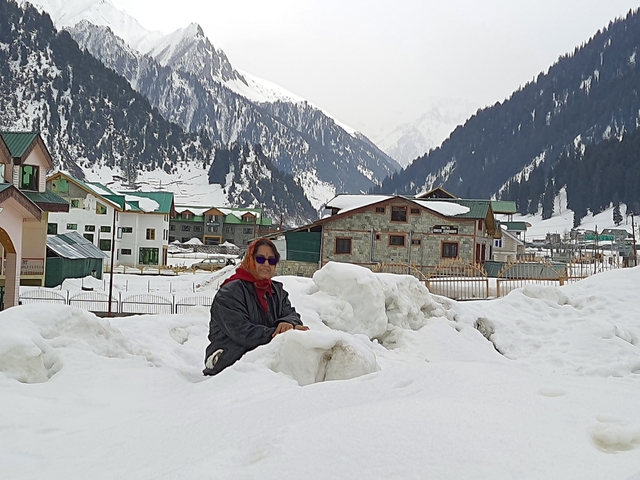 Person sitting in snow near mountain lodges.