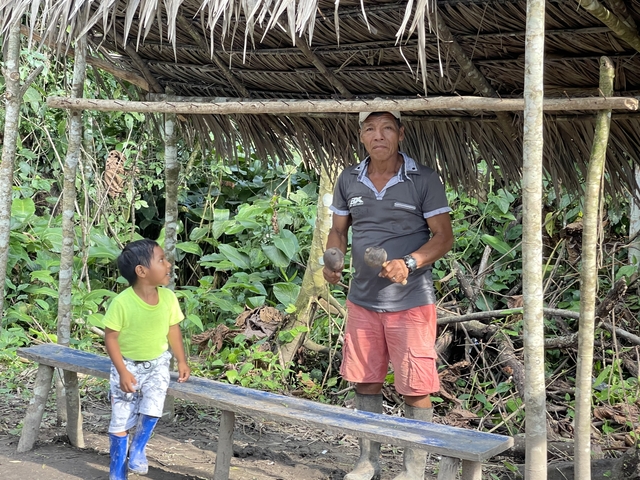 Elderly man and child standing under wooden shelter.