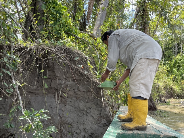 Person collecting soil sample by the river.
