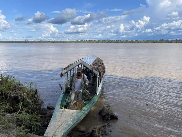 Man boarding a small boat at the riverbank.