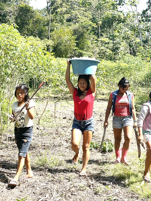 Women carrying a basket and holding tools in a rural area.
