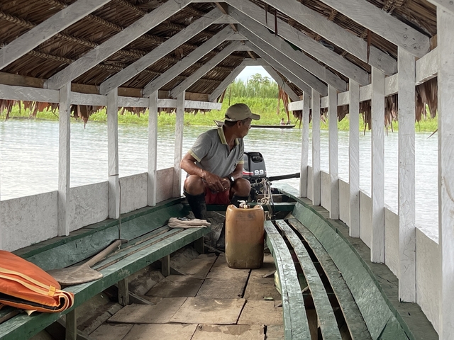 Man sitting in a covered boat on a river.