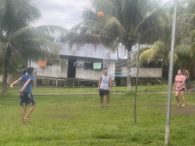 People playing volleyball on grass near a building.