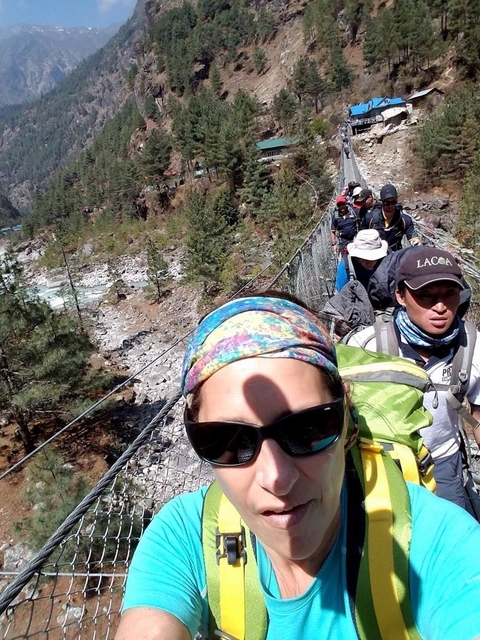 Trekkers crowded on a swaying suspension bridge high above a rocky Himalayan river valley.