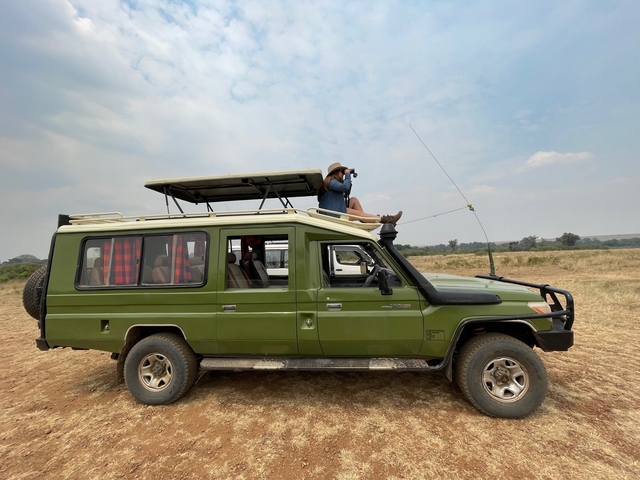 Person using binoculars on top of a safari vehicle.