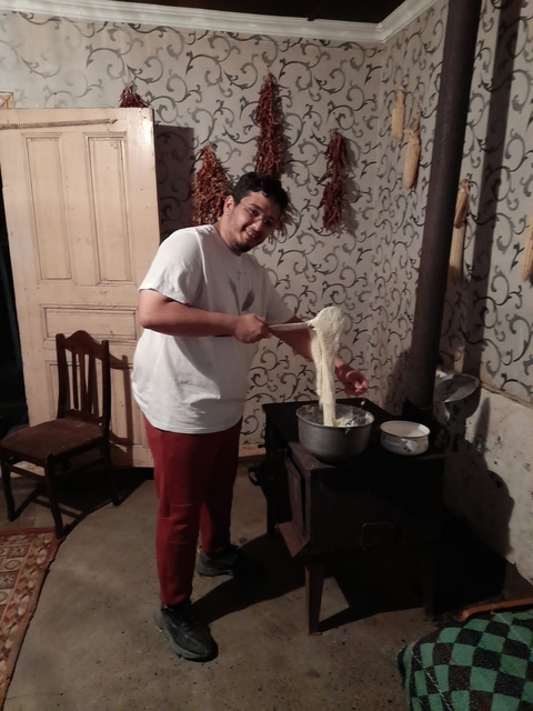 Person stirring a pot of traditional food inside a rustic kitchen.