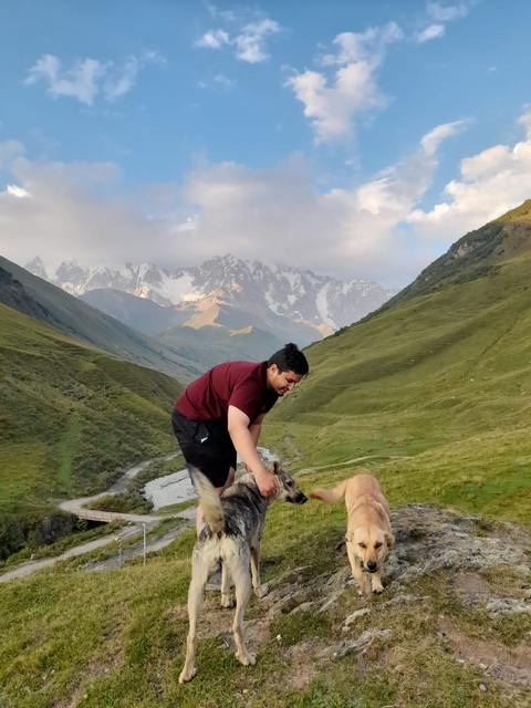 A person playing with a dog in a valley with mountains in the background.