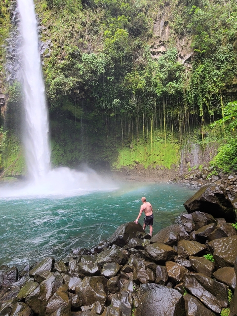 Man enjoying a waterfall in a lush forest.
